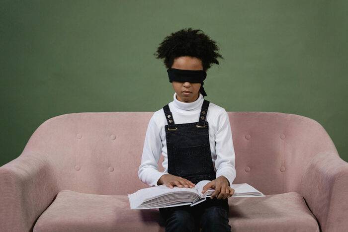 Picture of a small girl having the experience of reading while blindfolded